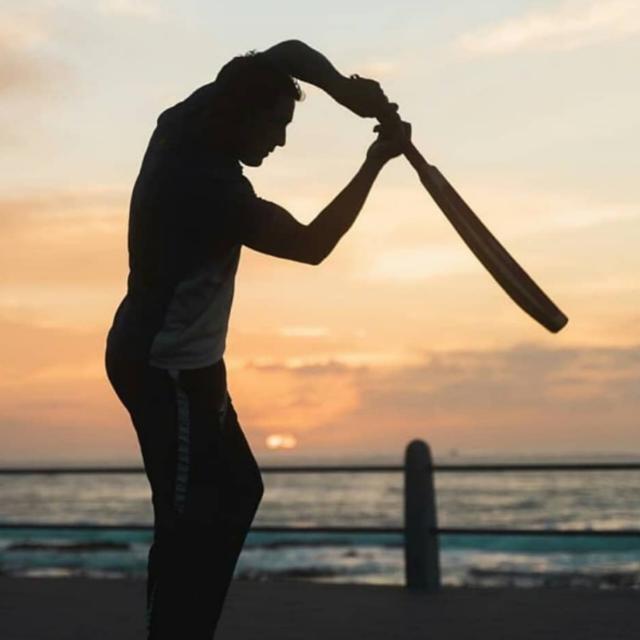 Brad Moses playing a cricket shot at sunset